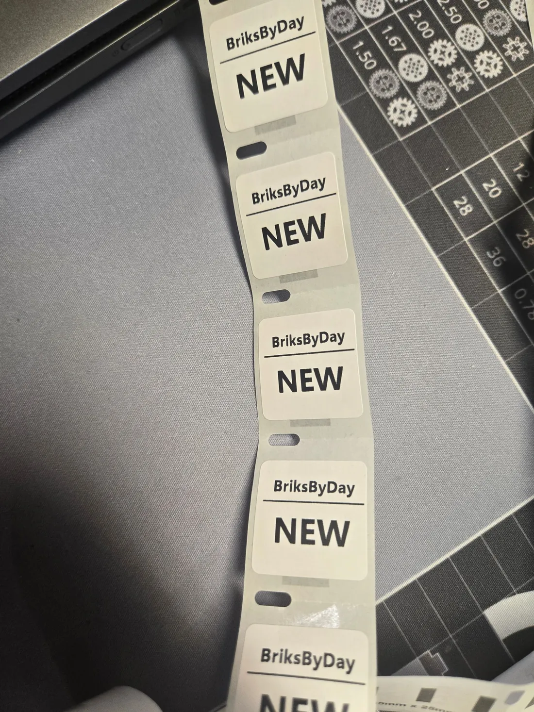 Strip of 1 x 1 inch labels printed NEW and BriksByDay, used inside orders to mark the bag of new parts