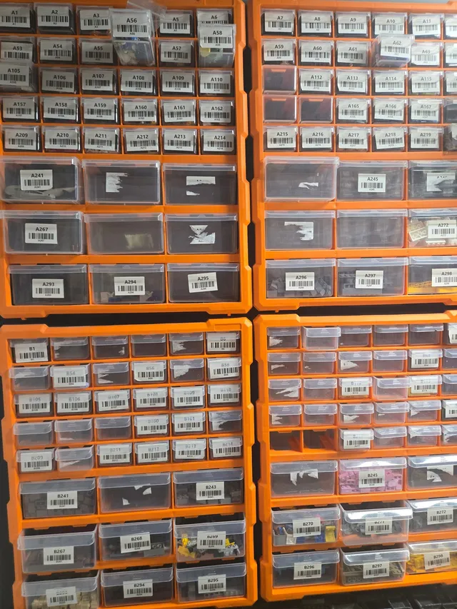 Four orange wall-mounted organizers in a 2x2 grid, with barcode-labeled clear drawers holding LEGO parts