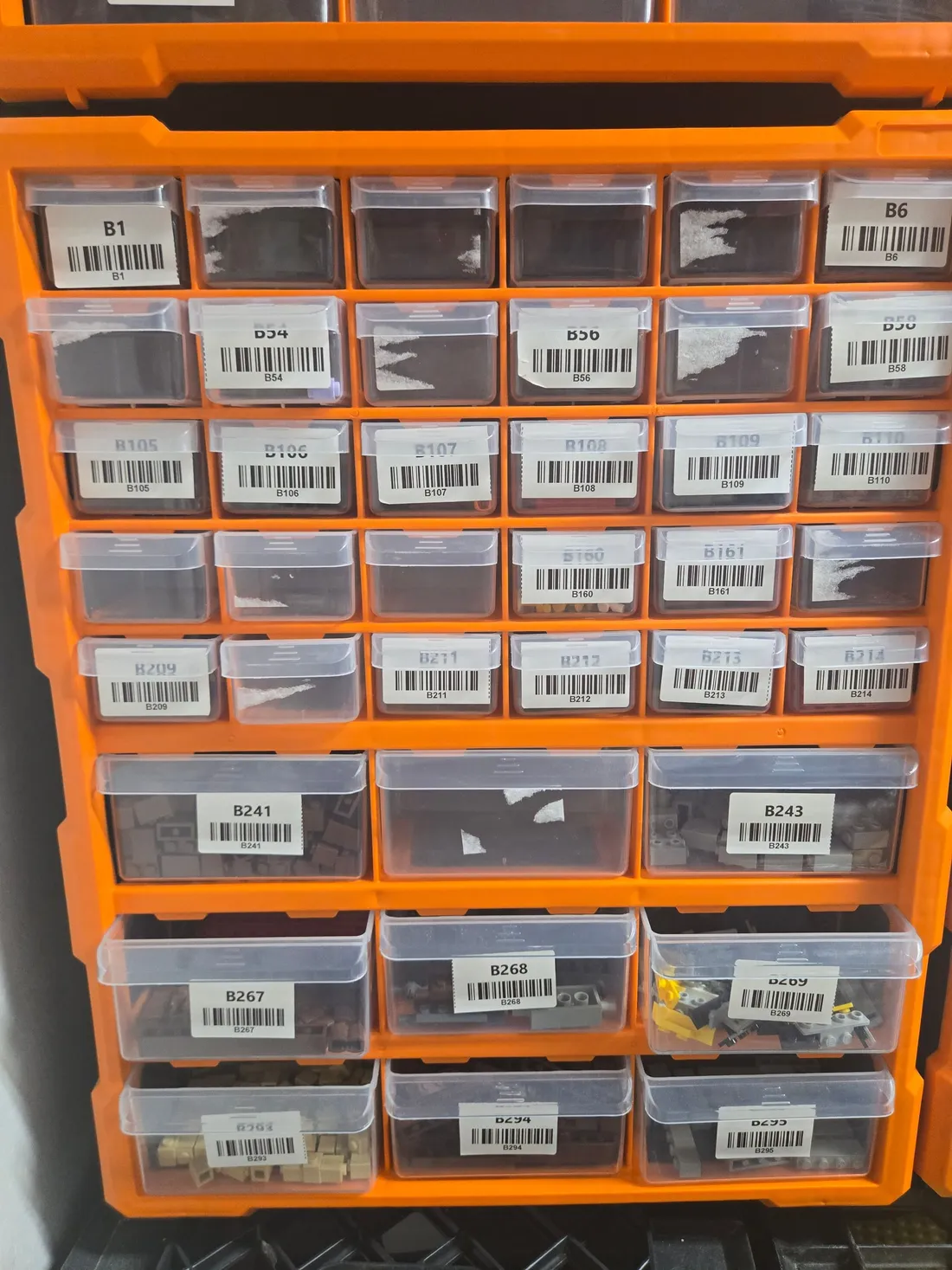 Orange wall-mount organizer with 30 small and 9 large clear drawers, many with barcode labels and LEGO parts