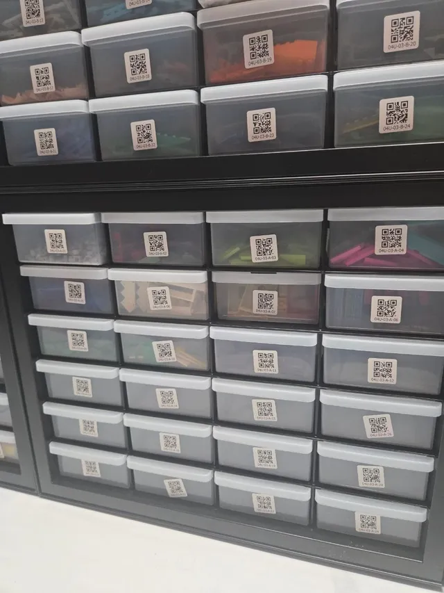 Stacked black 24-drawer cabinets with QR-code location labels on clear drawers of colorful LEGO parts