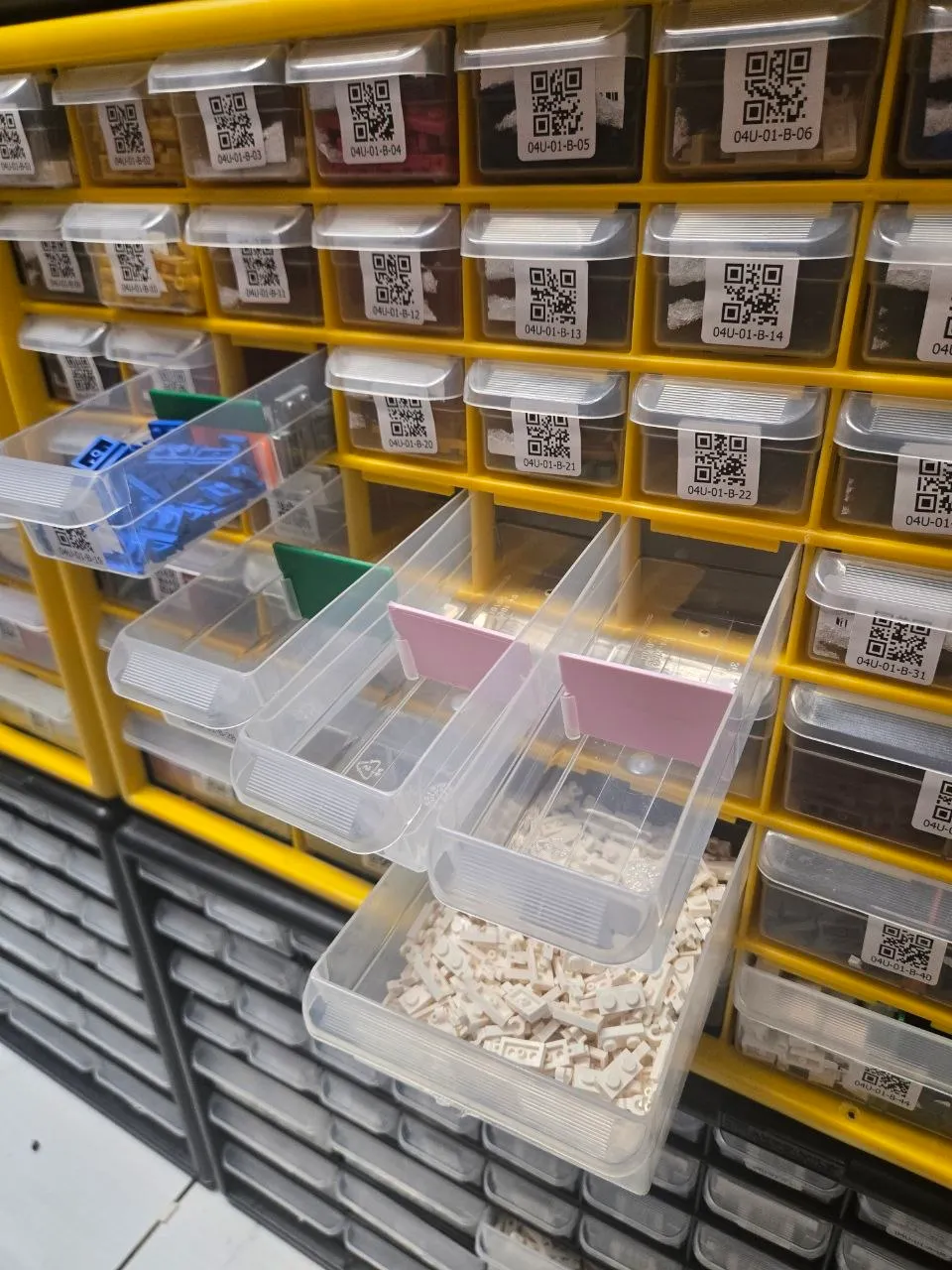 Yellow Akro-Mils cabinet with QR-labeled drawers, some pulled out showing dividers and white LEGO plates