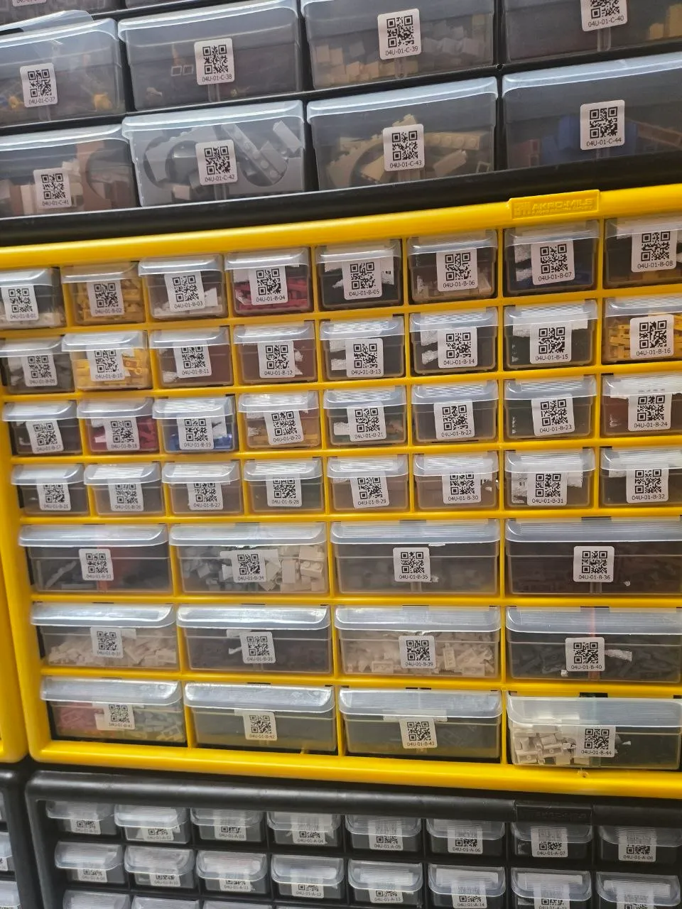 Yellow Akro-Mils 44-drawer cabinet holding LEGO parts, every drawer QR-labeled, between black cabinets