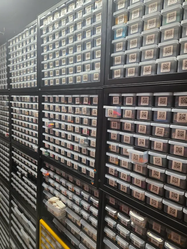 Wall of stacked black cabinets with hundreds of small clear drawers of LEGO parts, most with QR-code labels