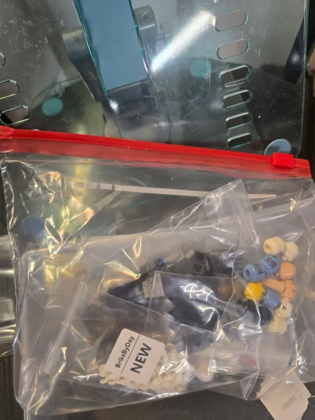 Clear red-slider bag holding smaller zip bags of minifigure heads and parts, one labeled BriksByDay NEW