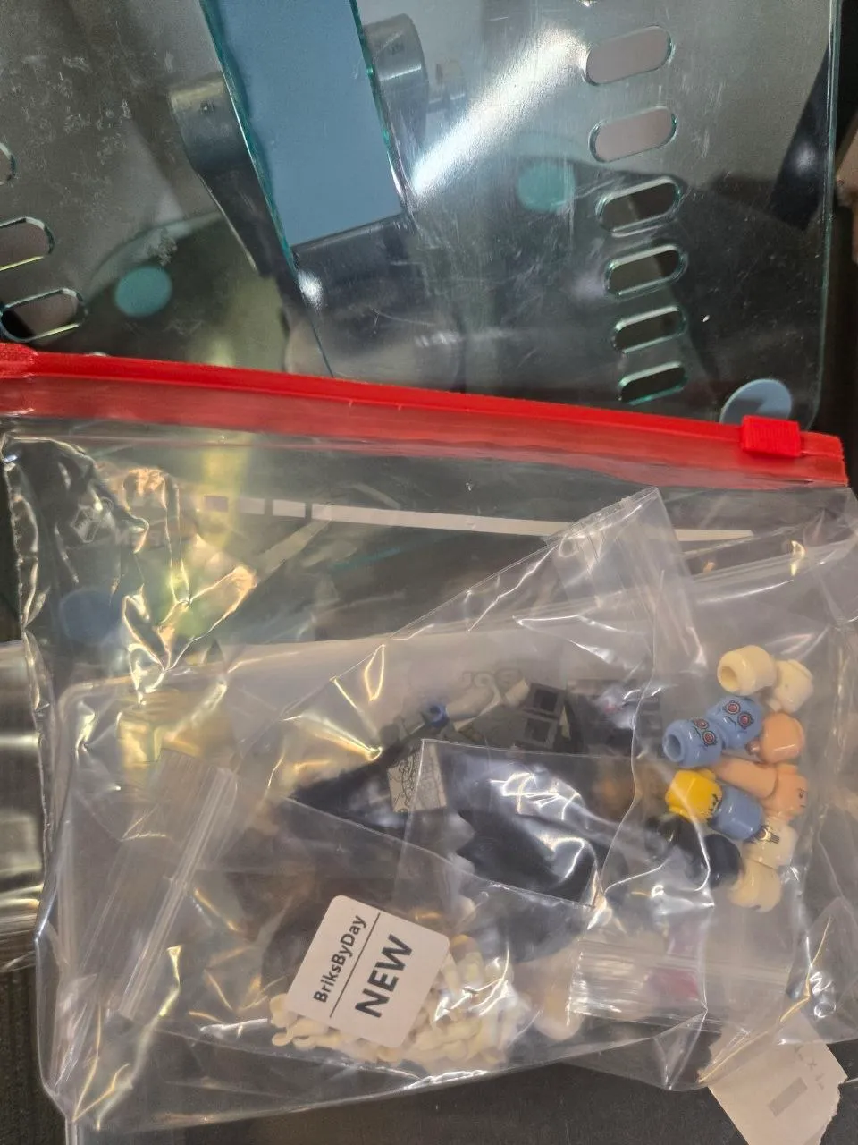 Clear red-slider bag holding smaller zip bags of minifigure heads and parts, one labeled BriksByDay NEW