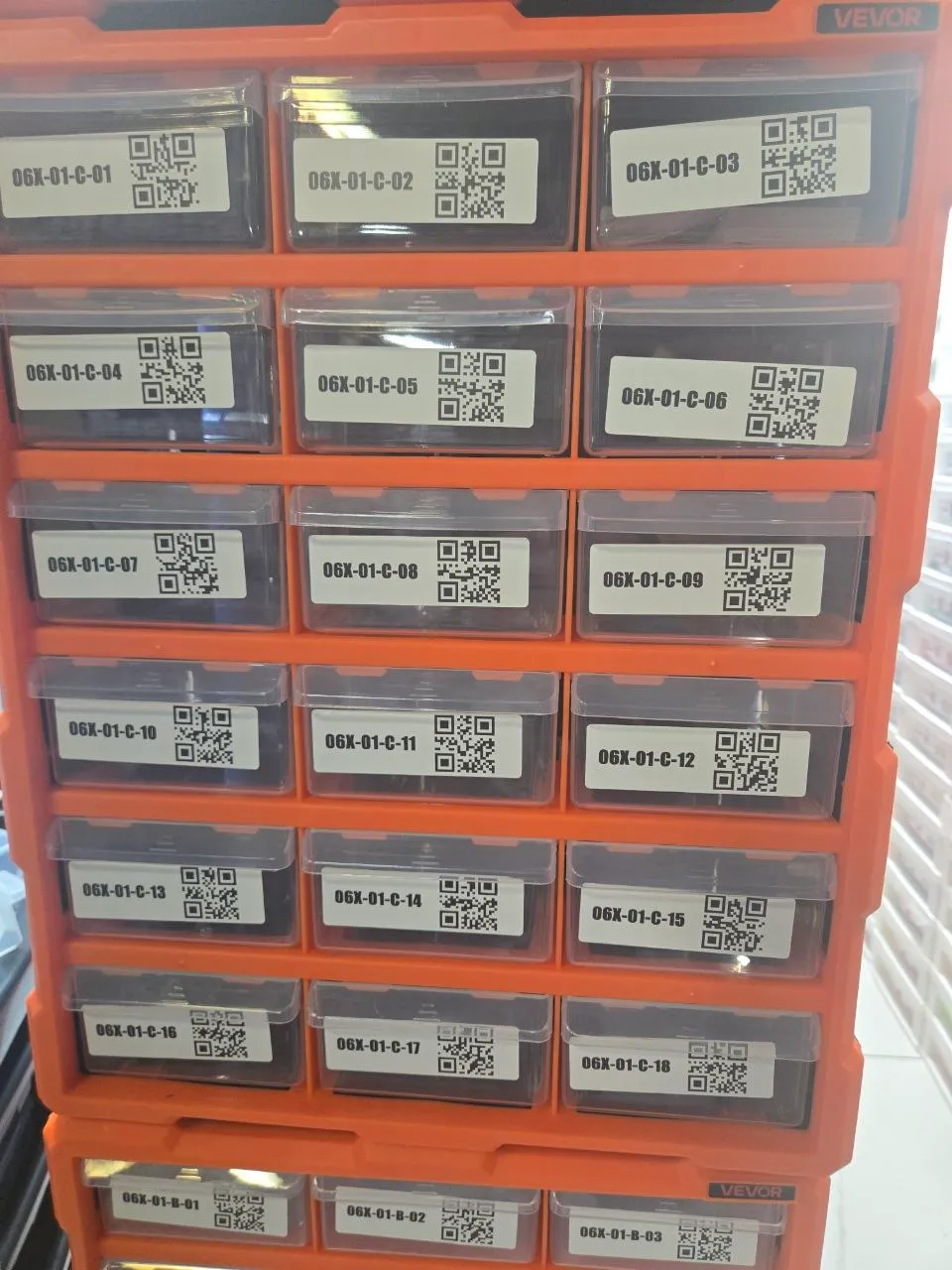 Front of an orange VEVOR 18-drawer cabinet, each clear drawer labeled with a location code and QR code