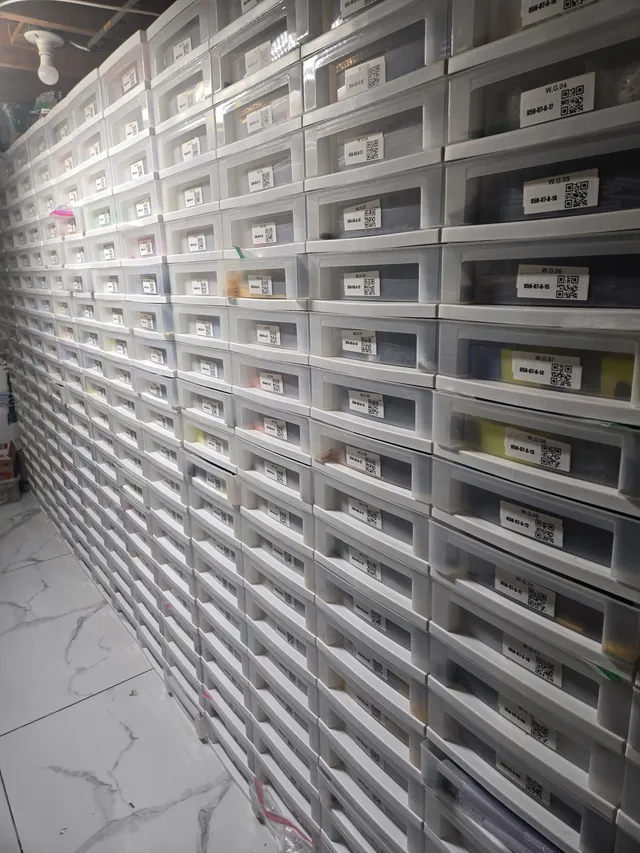 Long floor-to-ceiling wall of stacked white drawers of LEGO parts, each with a QR-code location label