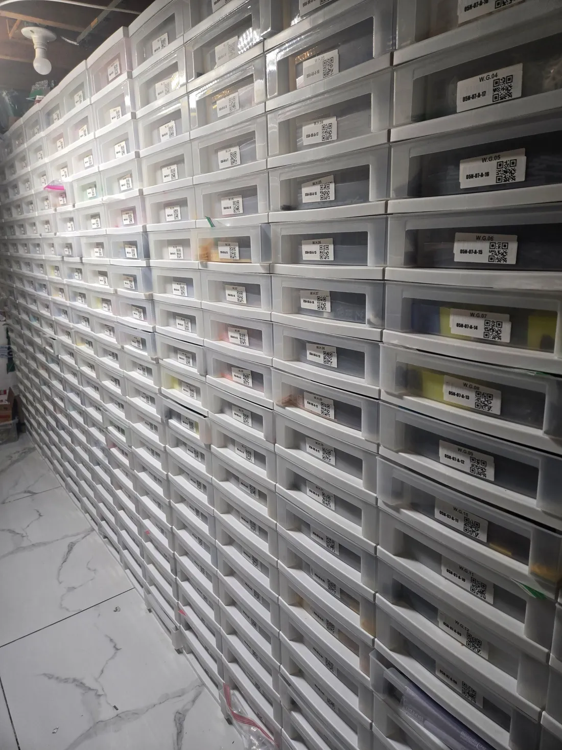 Long floor-to-ceiling wall of stacked white drawers of LEGO parts, each with a QR-code location label