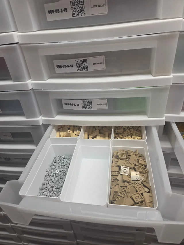 Open drawer split into six white 3D-printed bins of tan, dark tan and gray LEGO parts, one bin empty