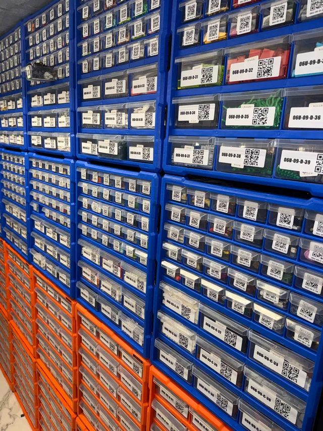 Wall of blue VEVOR 39-drawer organizers stacked on orange ones, every clear drawer carrying a QR-code location label