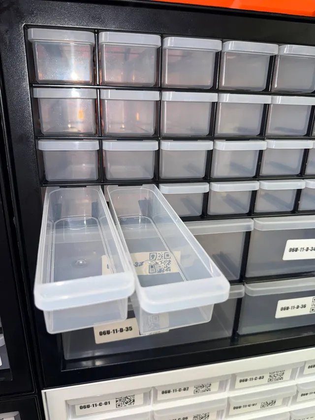 Two long, narrow drawers pulled out of a black IRIS 36-drawer cabinet, above its four large QR-labeled drawers